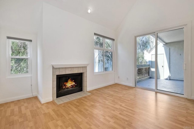 unfurnished living room featuring light wood finished floors, baseboards, a fireplace, and high vaulted ceiling