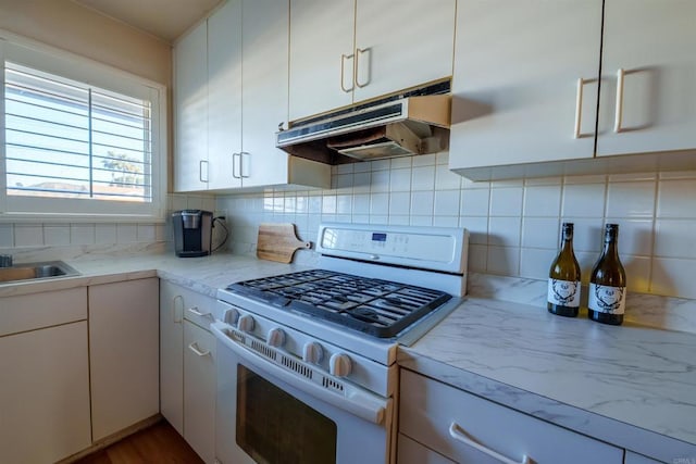 kitchen with light countertops, backsplash, white cabinets, white range with gas cooktop, and under cabinet range hood