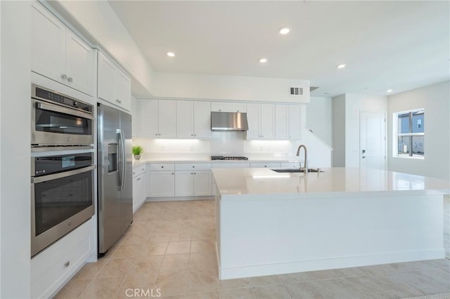 kitchen with appliances with stainless steel finishes, light countertops, under cabinet range hood, white cabinetry, and a sink