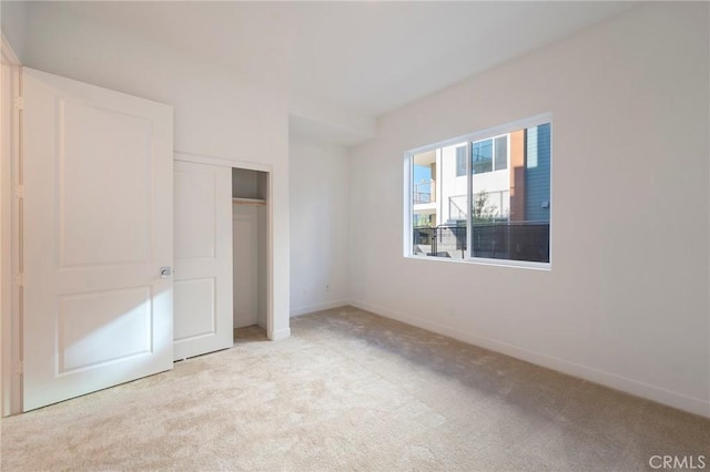 unfurnished bedroom with a closet, light carpet, and baseboards