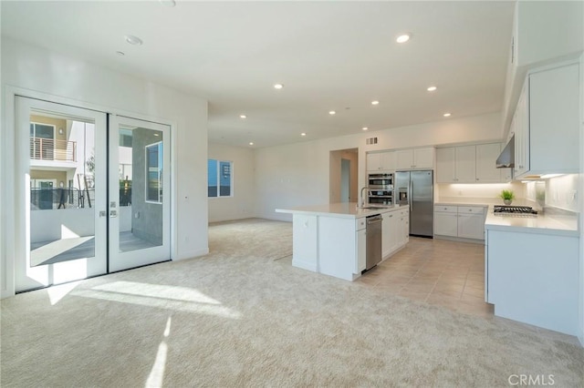 kitchen featuring range hood, light countertops, appliances with stainless steel finishes, light carpet, and a kitchen island with sink