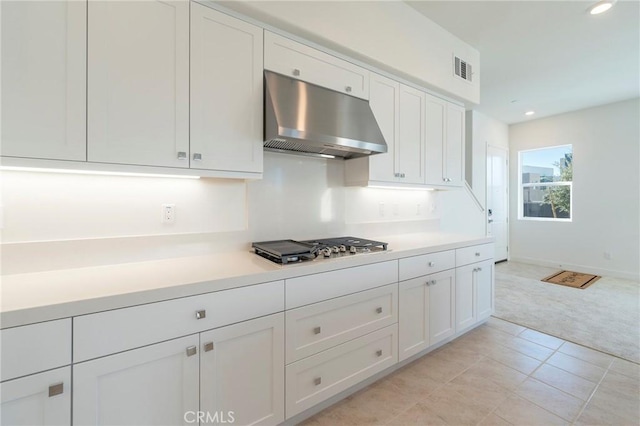 kitchen with under cabinet range hood, stainless steel gas cooktop, visible vents, white cabinets, and light countertops