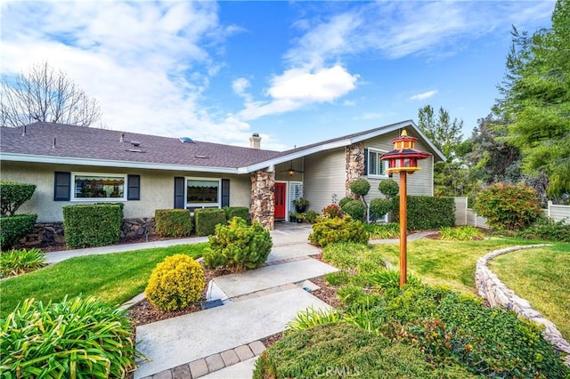 view of front of house with a shingled roof, a front yard, stone siding, and stucco siding