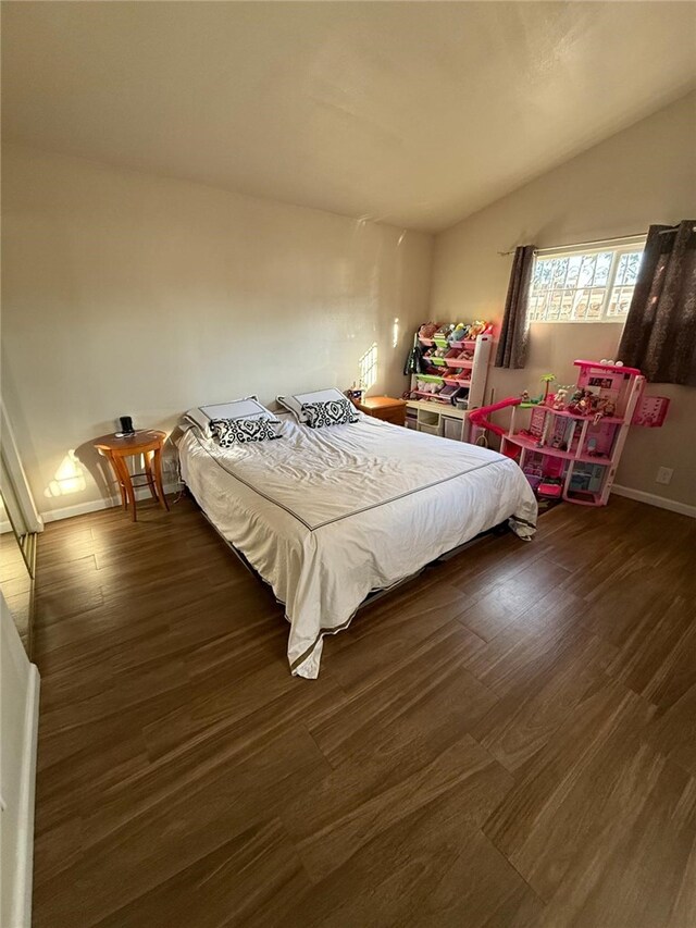 bedroom featuring dark wood-type flooring, vaulted ceiling, and baseboards