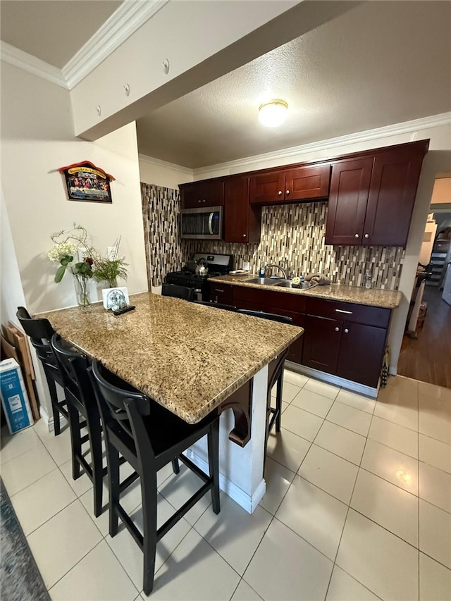 kitchen featuring stainless steel microwave, backsplash, black range with gas stovetop, ornamental molding, and a kitchen bar