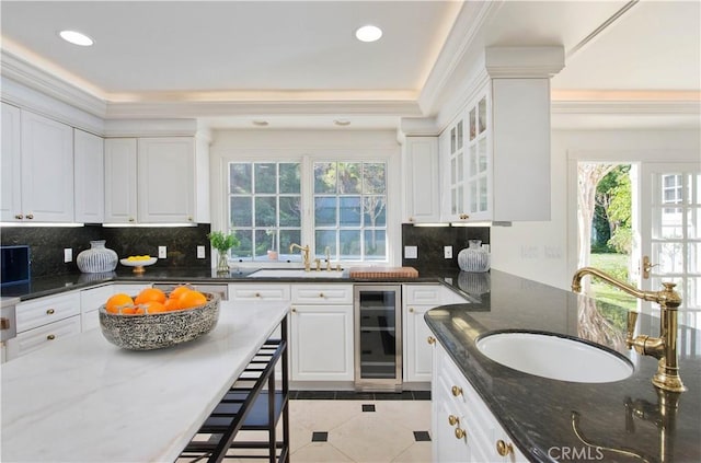 kitchen featuring tasteful backsplash, white cabinets, a sink, dark stone countertops, and beverage cooler