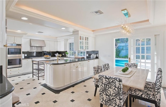 kitchen featuring visible vents, a raised ceiling, wall chimney exhaust hood, stainless steel double oven, and backsplash