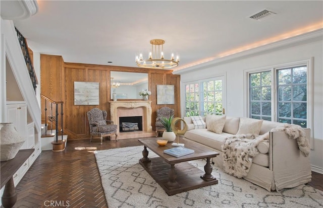 living room featuring visible vents, a premium fireplace, wooden walls, a chandelier, and stairs