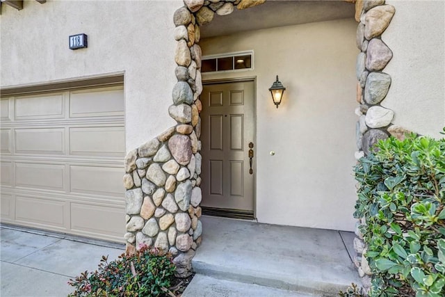 entrance to property featuring a garage, stone siding, and stucco siding