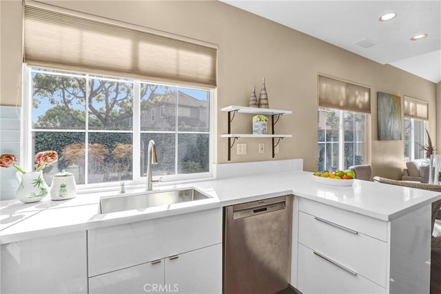 kitchen with a peninsula, a sink, white cabinets, light countertops, and dishwasher