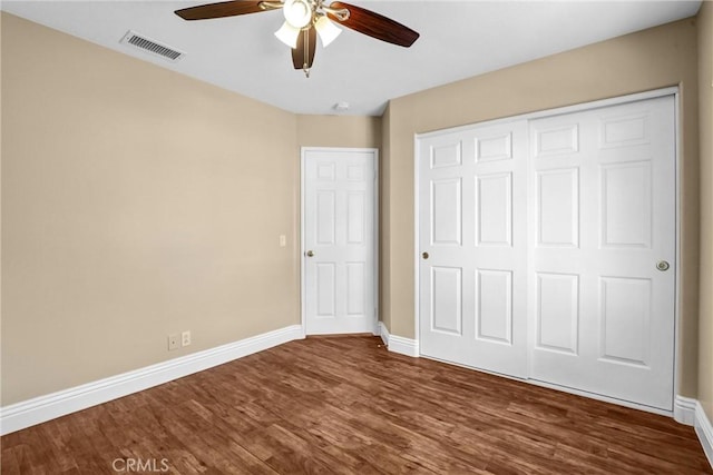 unfurnished bedroom featuring dark wood-style flooring, a closet, visible vents, ceiling fan, and baseboards