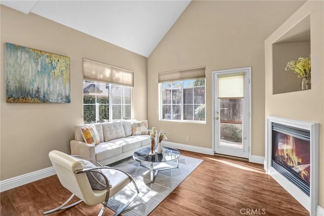 living area with high vaulted ceiling, baseboards, wood finished floors, and a glass covered fireplace