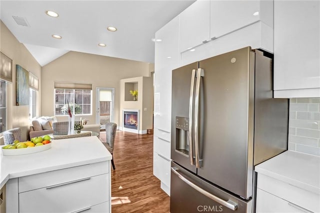 kitchen with white cabinets, open floor plan, light countertops, stainless steel refrigerator with ice dispenser, and a glass covered fireplace