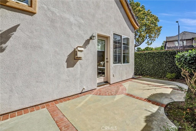 view of exterior entry featuring a patio area, fence, and stucco siding