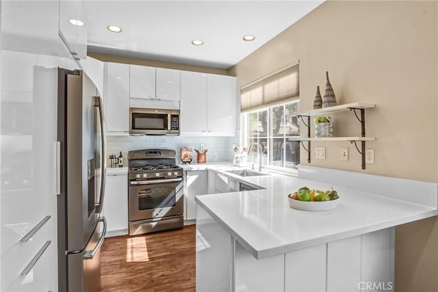 kitchen with tasteful backsplash, appliances with stainless steel finishes, white cabinets, a sink, and a peninsula