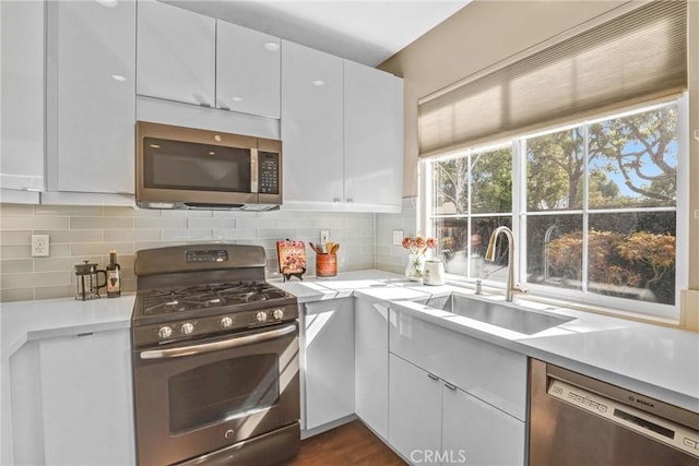 kitchen featuring stainless steel appliances, tasteful backsplash, light countertops, white cabinetry, and a sink