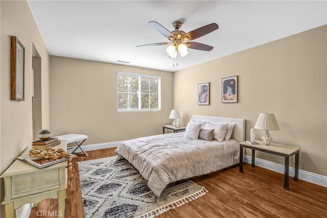 bedroom with a ceiling fan, visible vents, baseboards, and wood finished floors