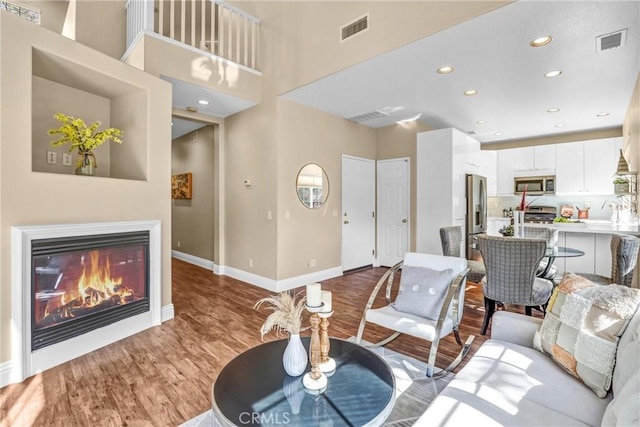 living room with baseboards, visible vents, wood finished floors, and a glass covered fireplace