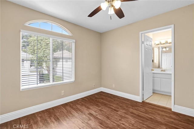 unfurnished bedroom featuring ceiling fan, ensuite bath, wood finished floors, and baseboards