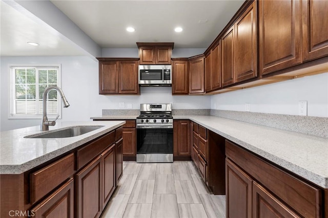 kitchen with light stone counters, recessed lighting, a sink, appliances with stainless steel finishes, and an island with sink