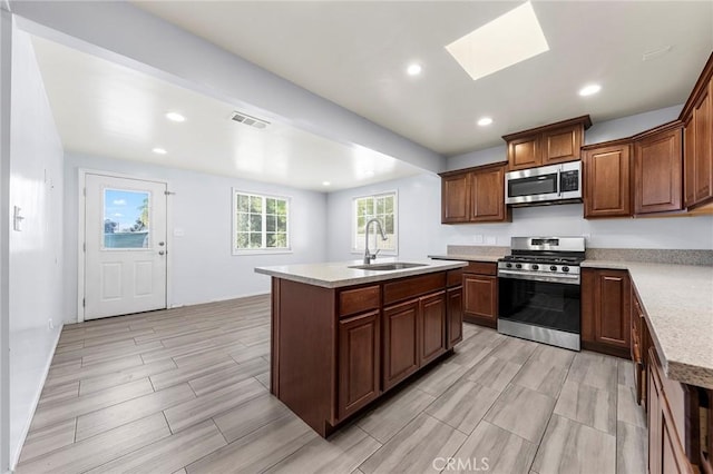 kitchen featuring stainless steel appliances, a skylight, a sink, visible vents, and an island with sink