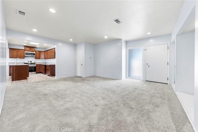 unfurnished living room with visible vents, a sink, and light colored carpet