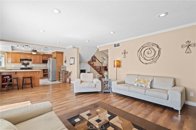 living room featuring light wood finished floors, visible vents, ornamental molding, and stairs