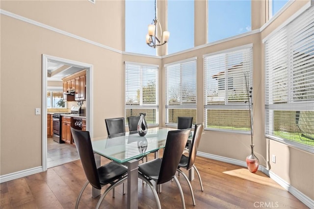 dining area with a high ceiling, baseboards, light wood-type flooring, and an inviting chandelier