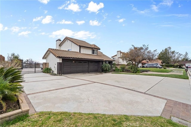 view of side of property featuring a tiled roof, stucco siding, a garage, driveway, and a gate