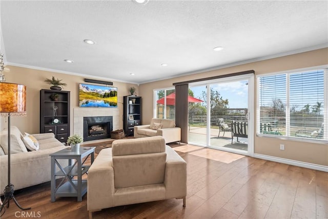 living area with crown molding, baseboards, recessed lighting, a fireplace, and wood-type flooring