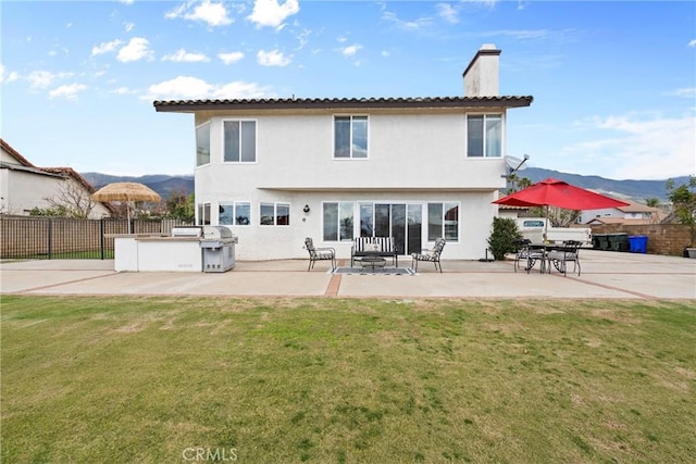 back of house with fence, stucco siding, a chimney, a yard, and a patio area