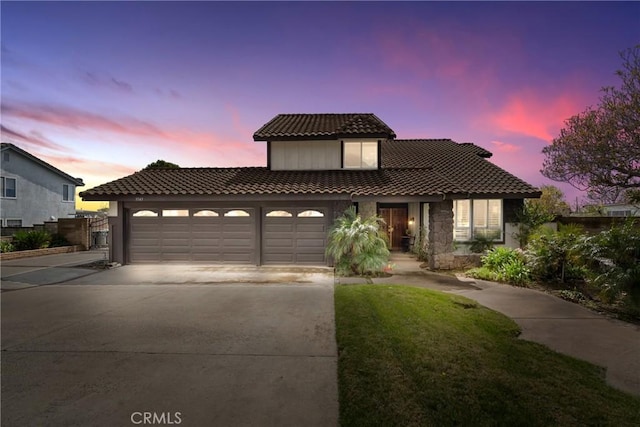 mediterranean / spanish-style home with stone siding, a garage, a tiled roof, concrete driveway, and a yard