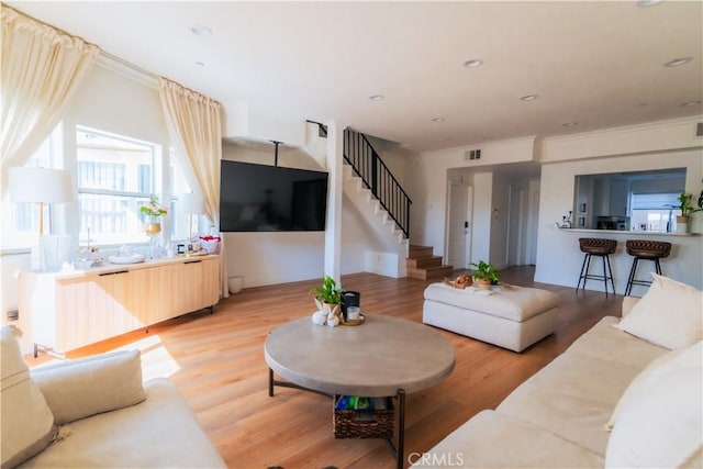 living area with ornamental molding, light wood-type flooring, visible vents, and stairs