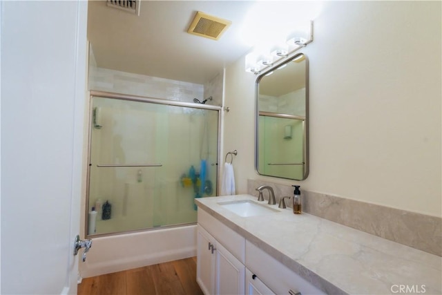 bathroom with bath / shower combo with glass door, wood finished floors, vanity, and visible vents