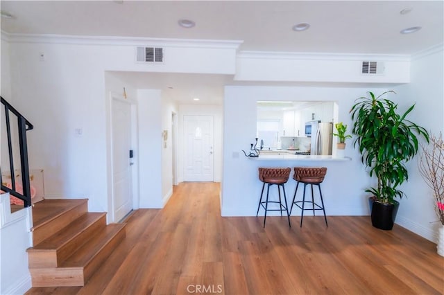 kitchen with light wood-style flooring, a breakfast bar, visible vents, white cabinetry, and freestanding refrigerator