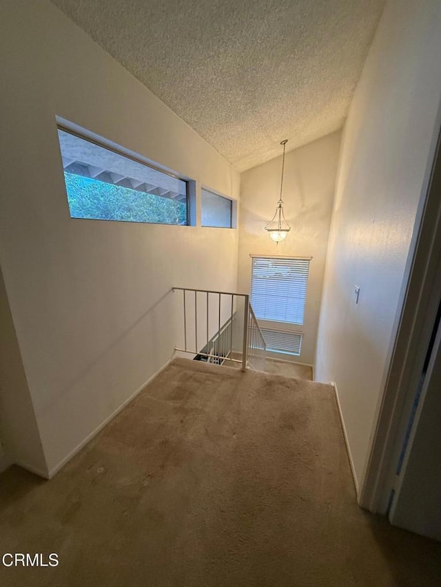 hallway with carpet flooring, vaulted ceiling, a textured ceiling, and an upstairs landing