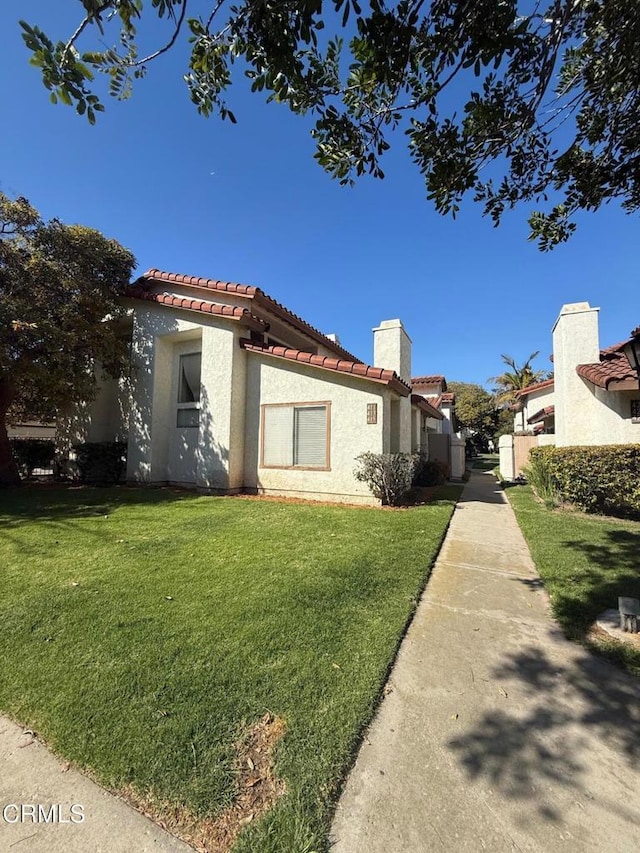 view of side of home featuring a lawn, a tiled roof, and stucco siding