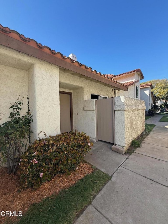 entrance to property featuring a gate, a tiled roof, and stucco siding