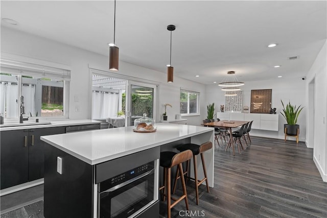 kitchen with dark wood-style floors, decorative light fixtures, light countertops, dark cabinetry, and a sink