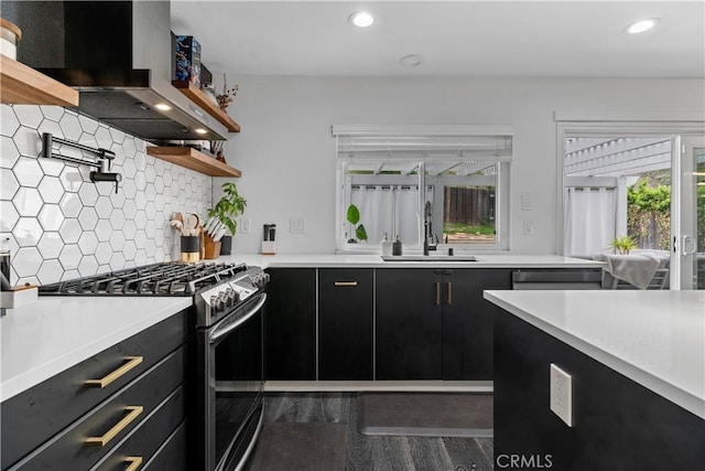 kitchen featuring a sink, light countertops, dark cabinetry, wall chimney range hood, and stainless steel range with gas cooktop