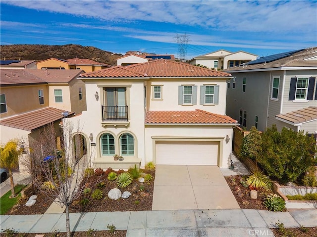 mediterranean / spanish-style home with concrete driveway, a tiled roof, a balcony, and stucco siding