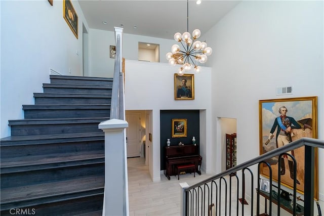 stairs with high vaulted ceiling, wood finished floors, visible vents, and a notable chandelier