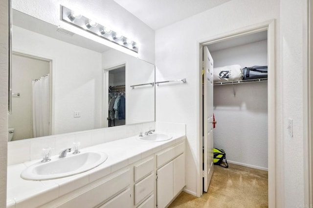 full bath with double vanity, a spacious closet, baseboards, and a sink