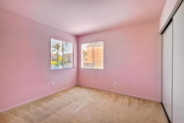 unfurnished bedroom with a closet, light colored carpet, and baseboards