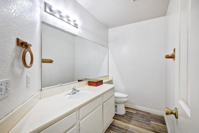 bathroom featuring toilet, baseboards, wood finished floors, and vanity