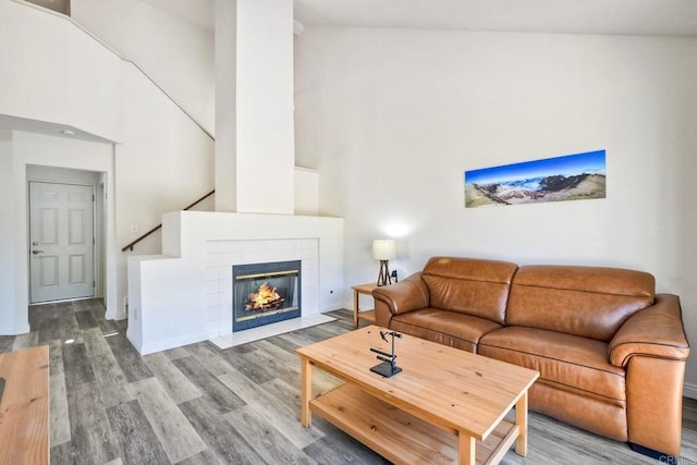 living area featuring a tile fireplace, a towering ceiling, baseboards, and wood finished floors