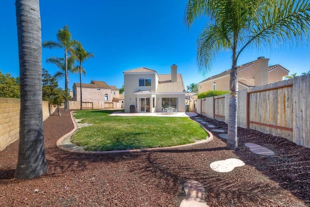 rear view of house with a fenced backyard, a yard, stucco siding, a chimney, and a patio area