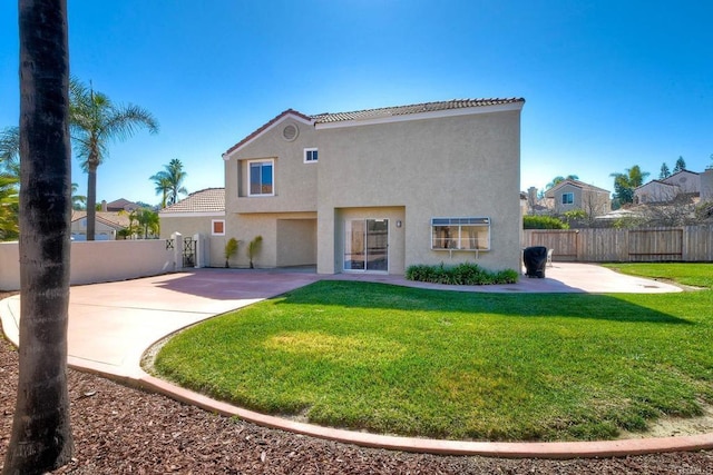 rear view of property featuring fence, a yard, a tiled roof, stucco siding, and a patio area