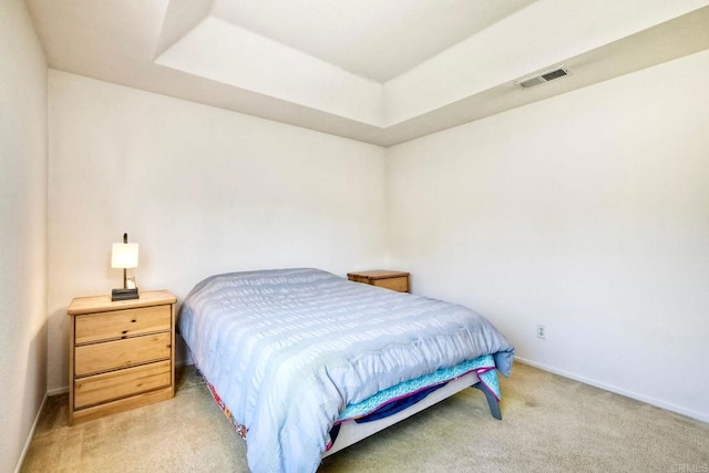 bedroom with light carpet, a tray ceiling, visible vents, and baseboards