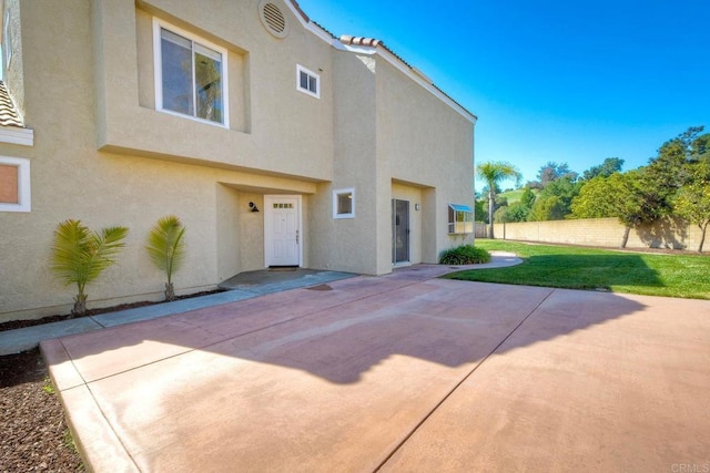 rear view of house featuring fence, a tile roof, a lawn, stucco siding, and a patio area